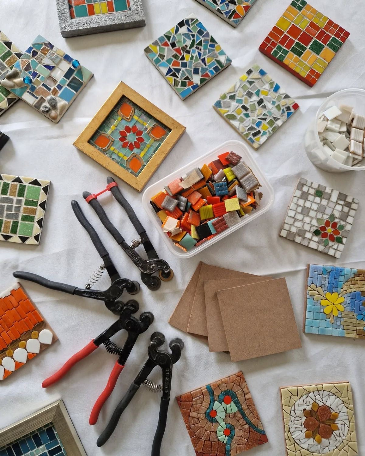 Collection of mosaic tiles, tools, and materials on a white surface